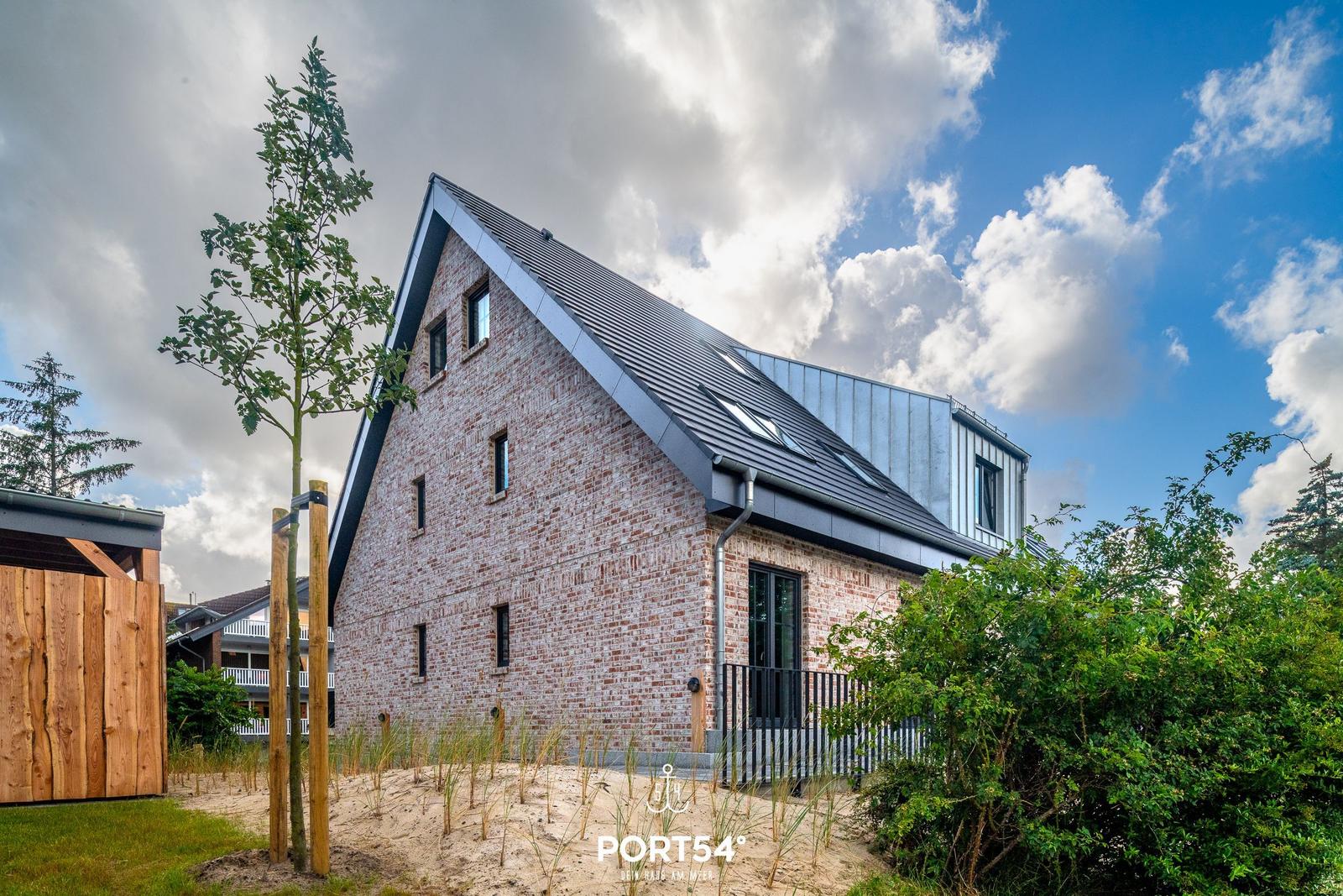 Moderne Villa mit Holzterrasse und Dachfenstern unter blauem Himmel.