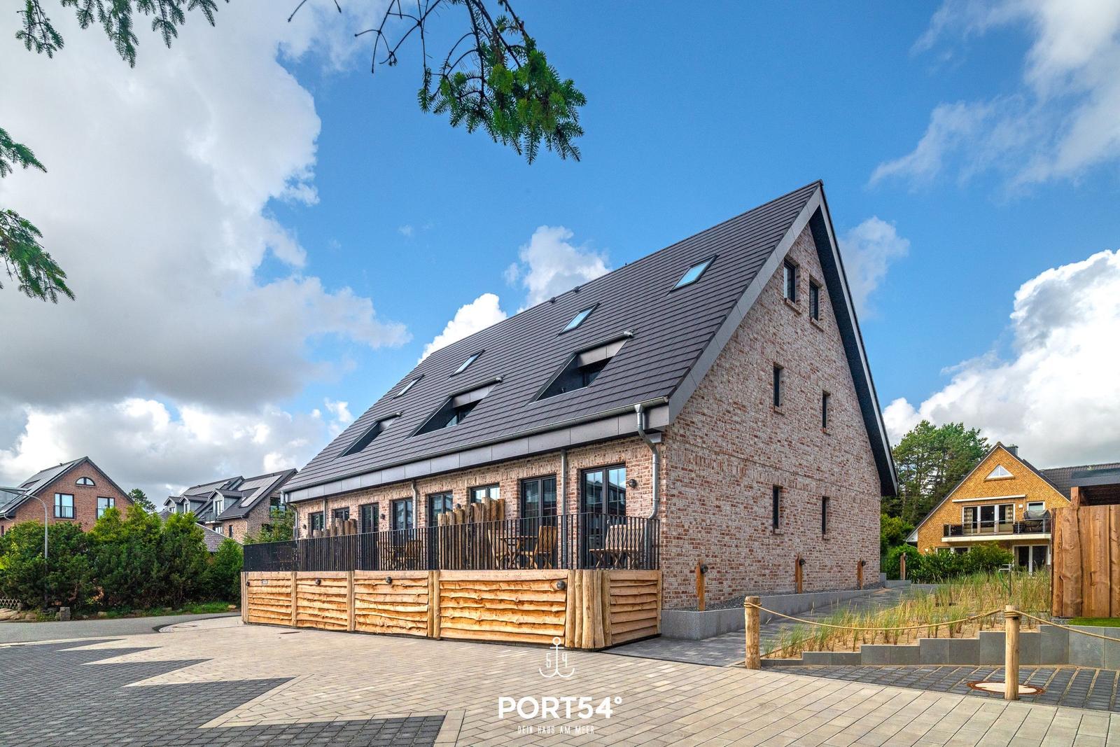 Modernes Backsteinhaus mit Dachterrasse und Gartenbereich unter blauem Himmel.