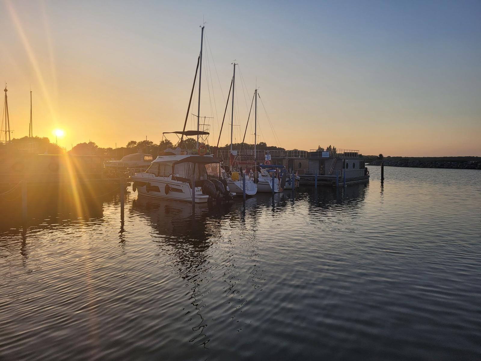 Sonnenuntergang am Hafen mit mehreren Booten und einem Hausboot.