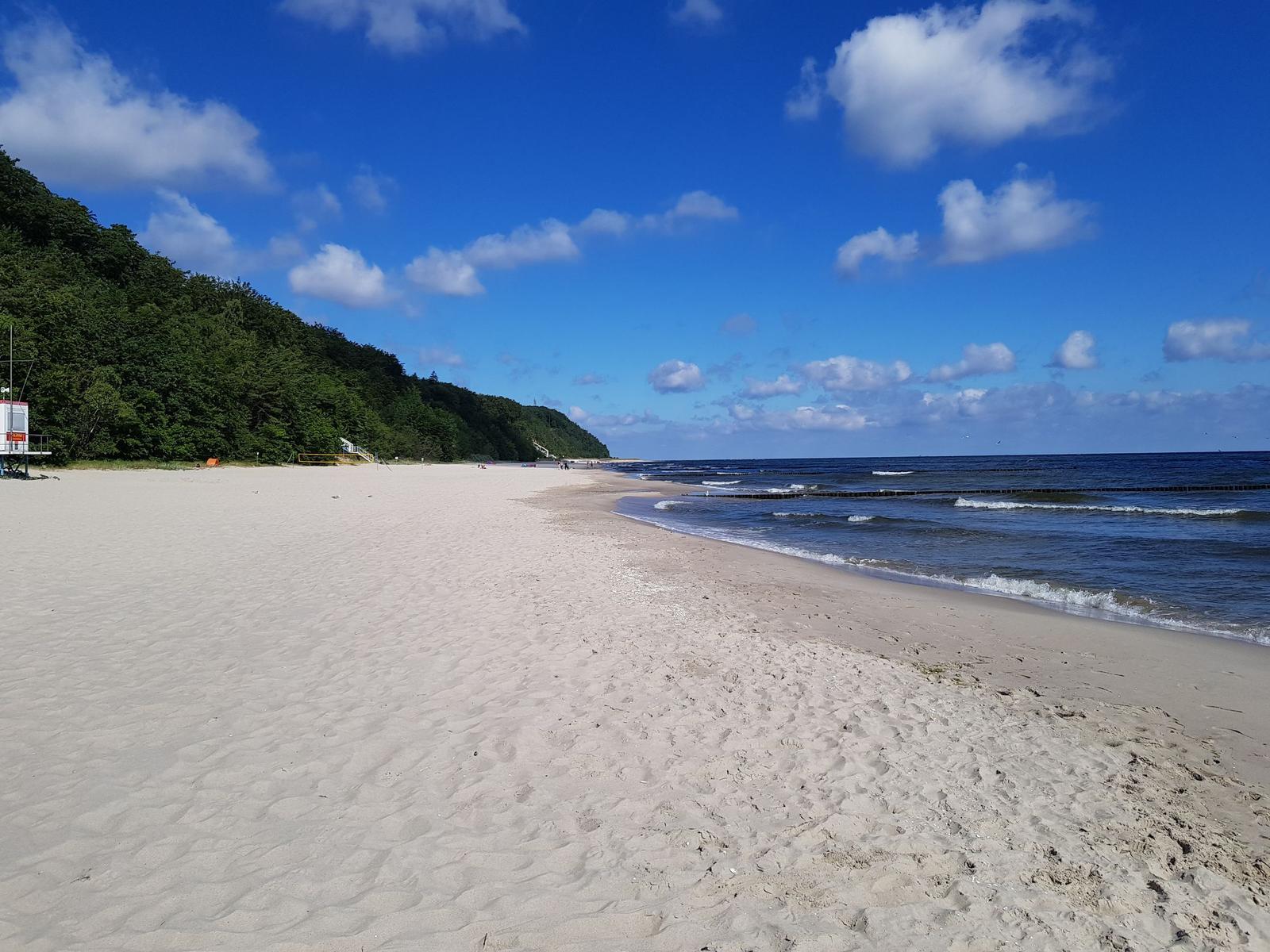 Weiterer Sandstrand mit Blick auf das Meer und grüne Hügel im Hintergrund.