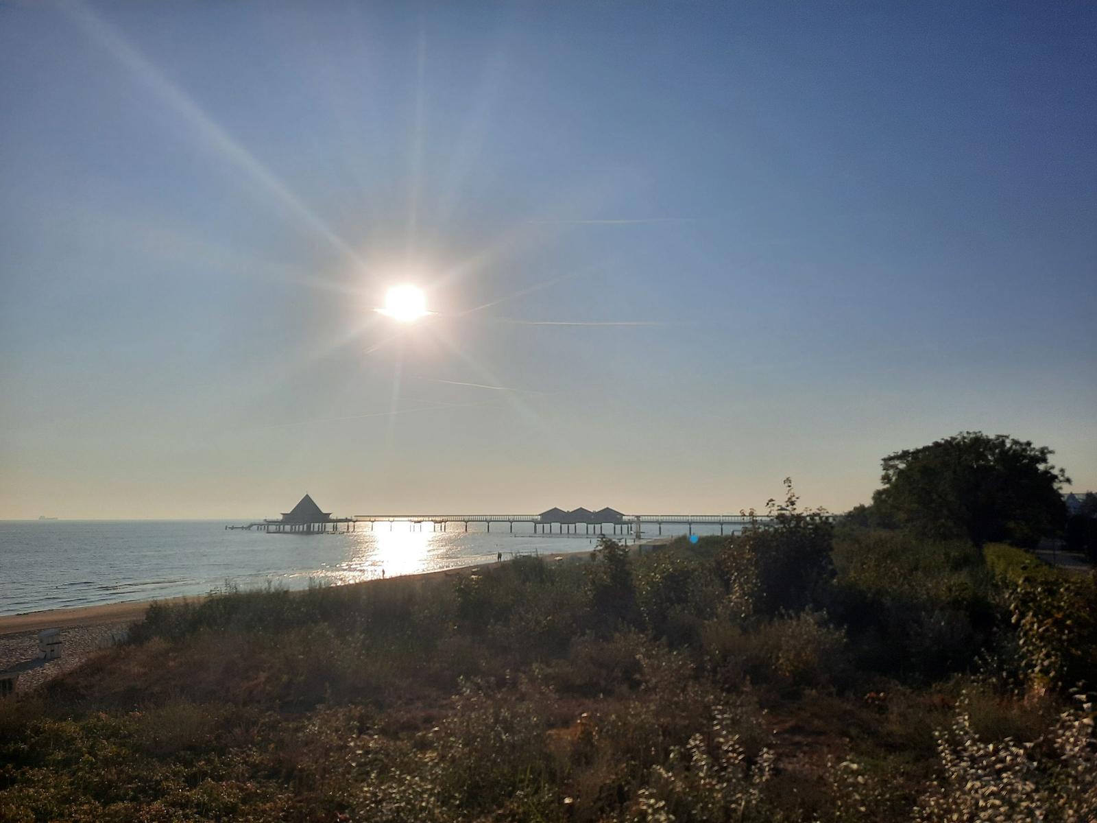 Ein gepflasterter Weg mit Bänken und Bäumen führt zum Strand.