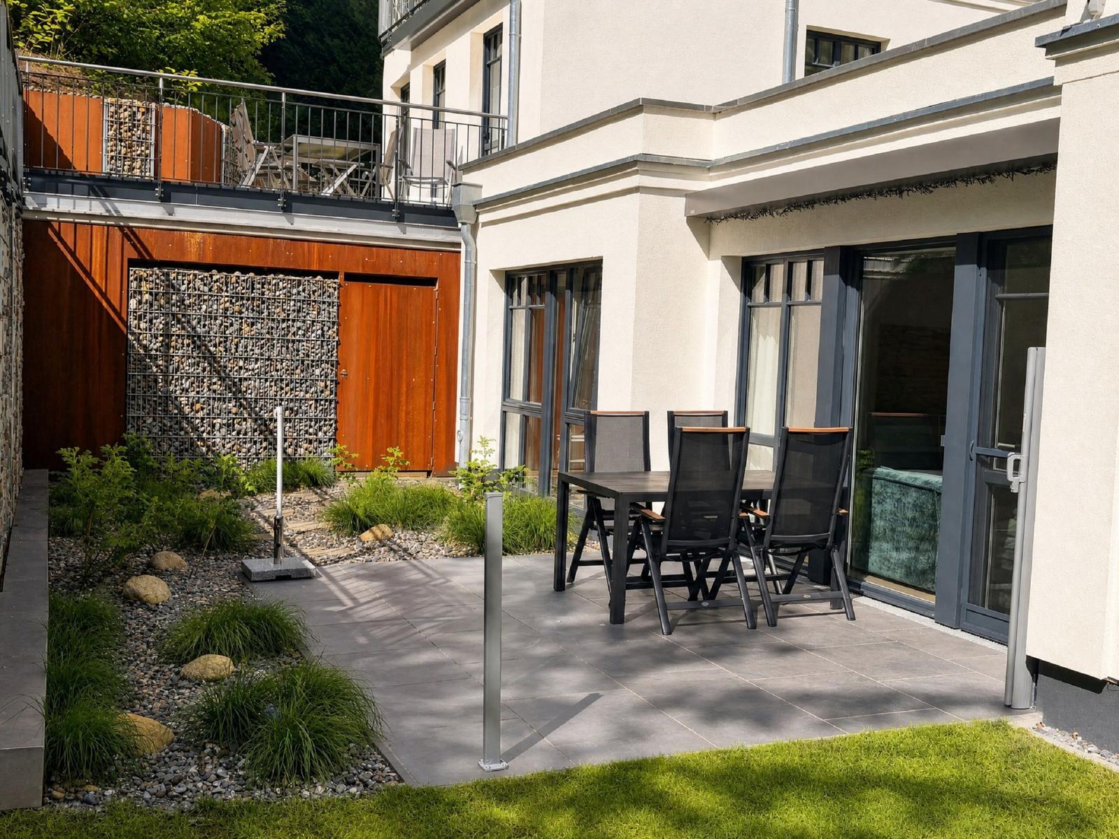 Wohnzimmer mit Sofa, Couchtisch und TV. Durchgang zur Terrasse mit Garten.