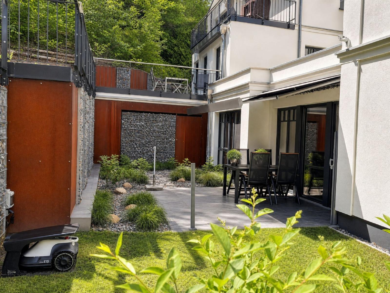 Terrasse mit Tisch und Stühlen, angrenzender Garten mit Rasen und Pflanzen.