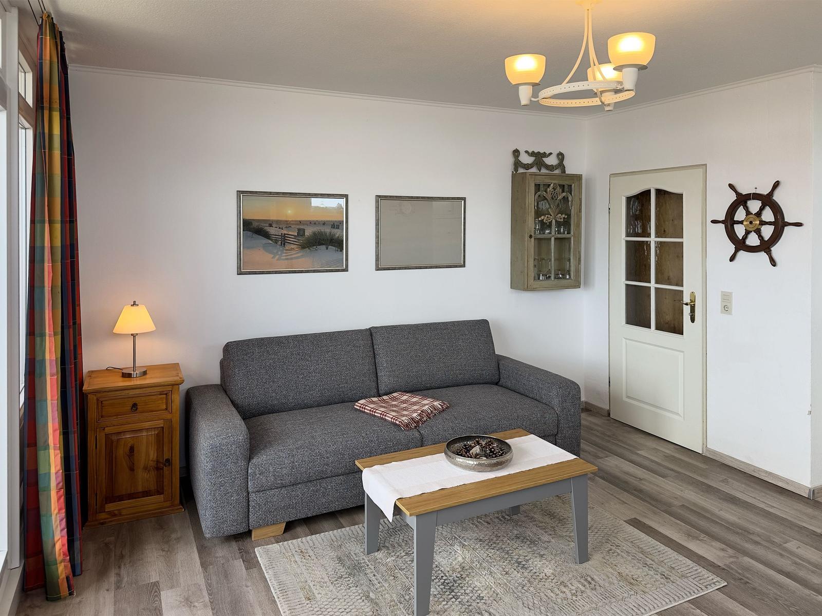 Wohnzimmer mit Sofa, Sessel und Balkonblick auf Dächer