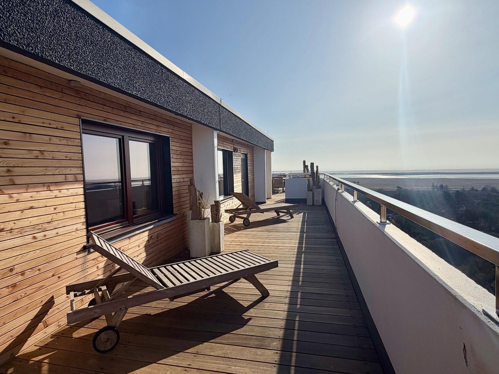 Terrasse mit Holztisch und Stühlen, Blick auf Meer und Strand.