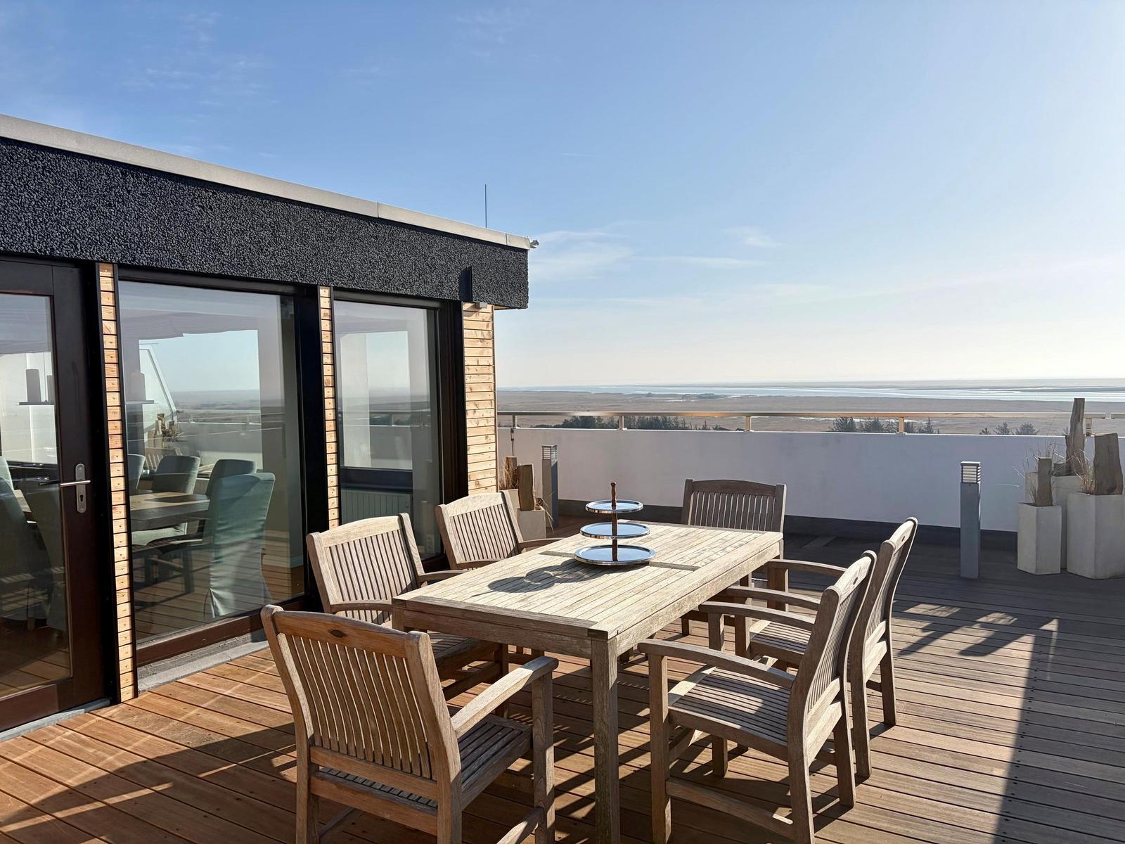 Terrasse mit Holzbank und Pflanzen, Blick auf Wald und Horizont.