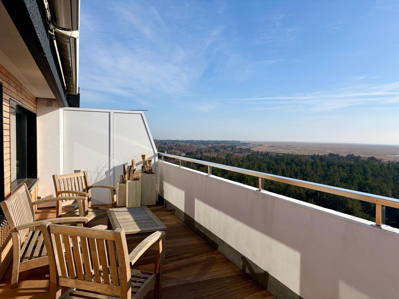 Terrasse mit Holztisch und Stühlen, Blick auf Meer und Horizont.