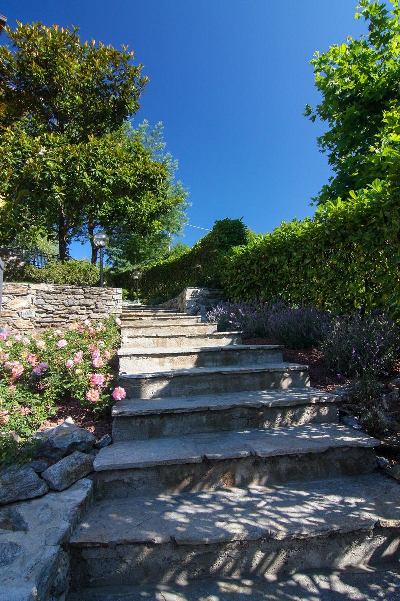 Steinweg führt durch grüne Wiesen und Obstbäume unter blauem Himmel.