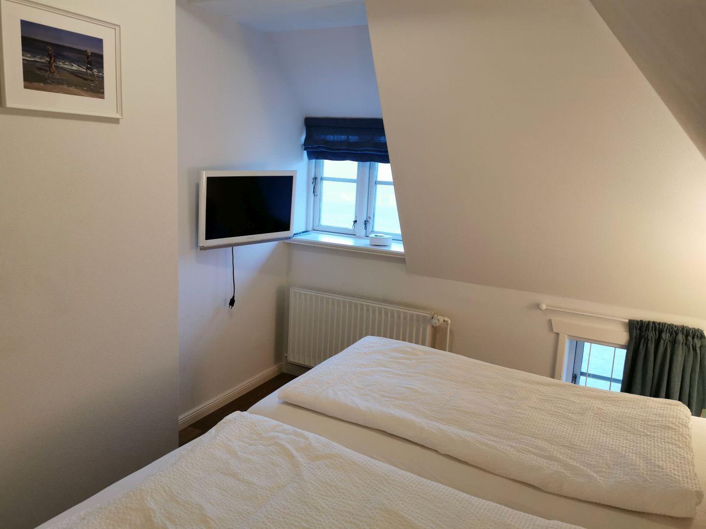 Zwei Betten in einem Dachzimmer mit weißen Laken und einer Wandlampe.