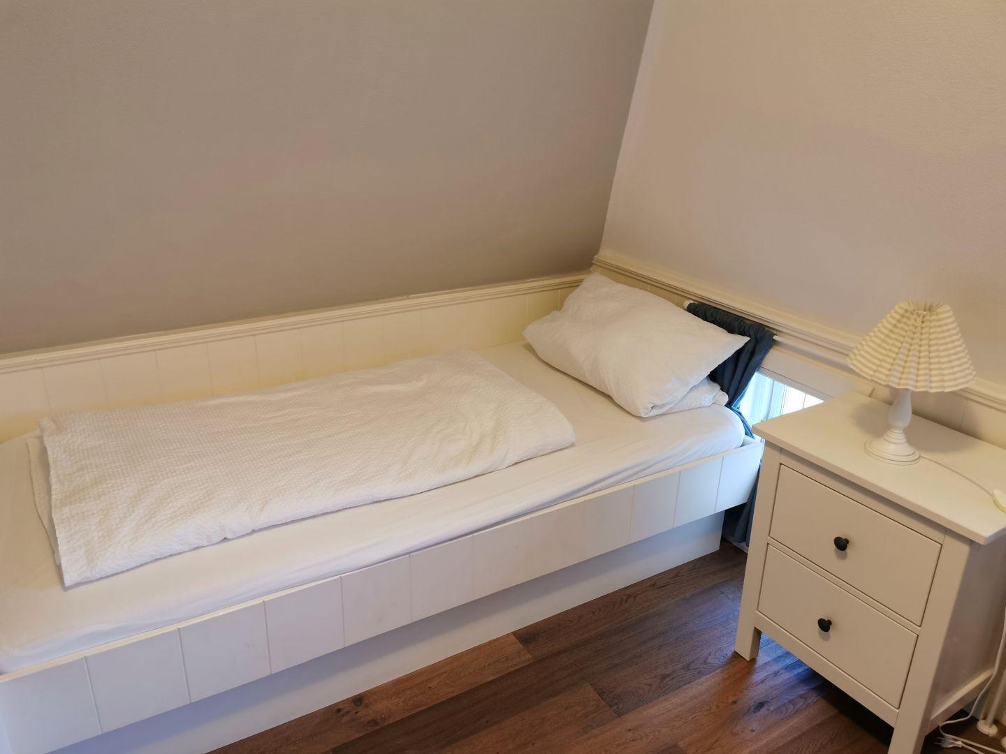 Zimmer mit rotem Schrank, weißem Nachttisch und Segelschiffmodell.