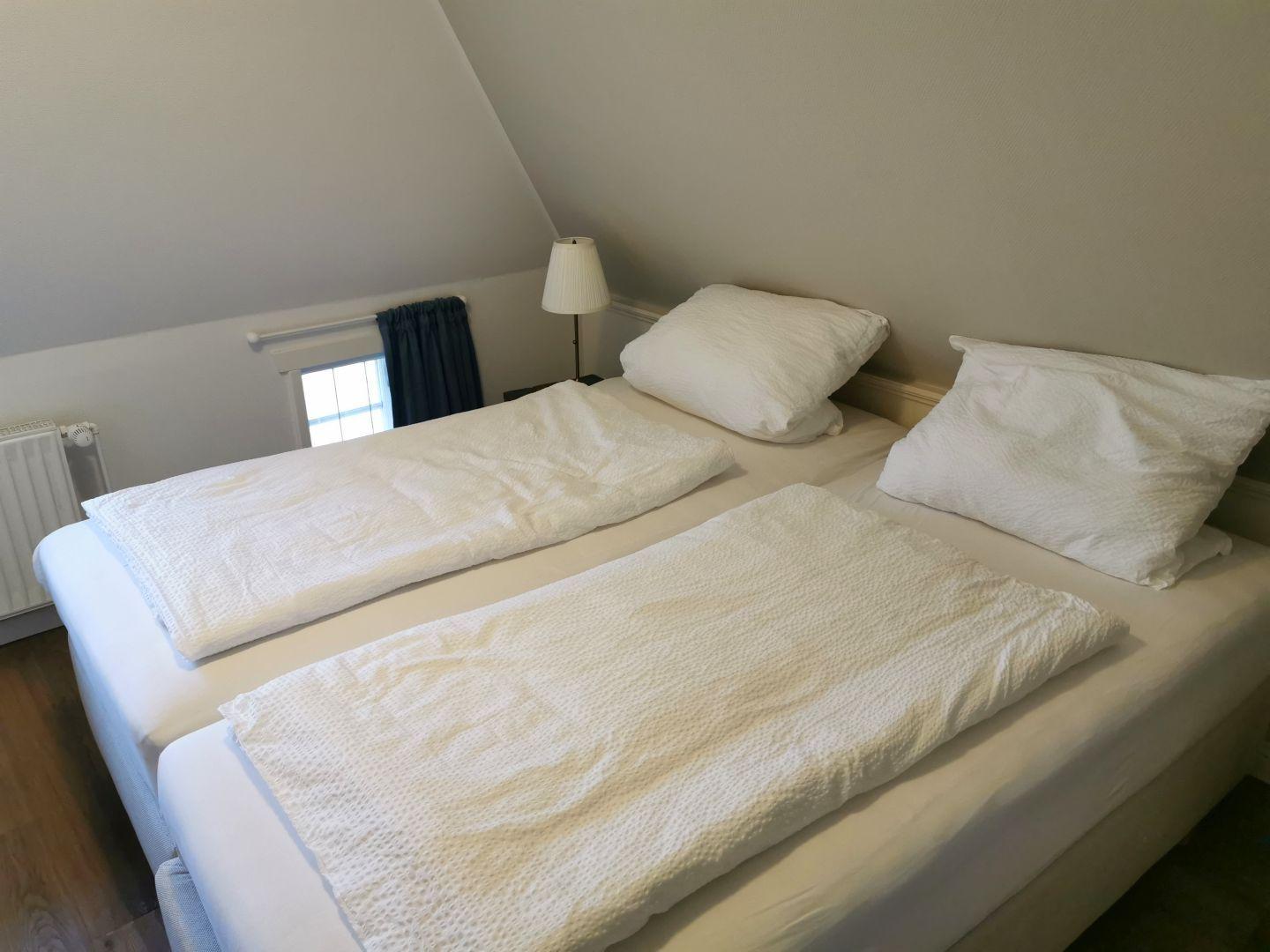 Schlafzimmer mit Dachschrägen, Bett, Fernseher und Fenster.