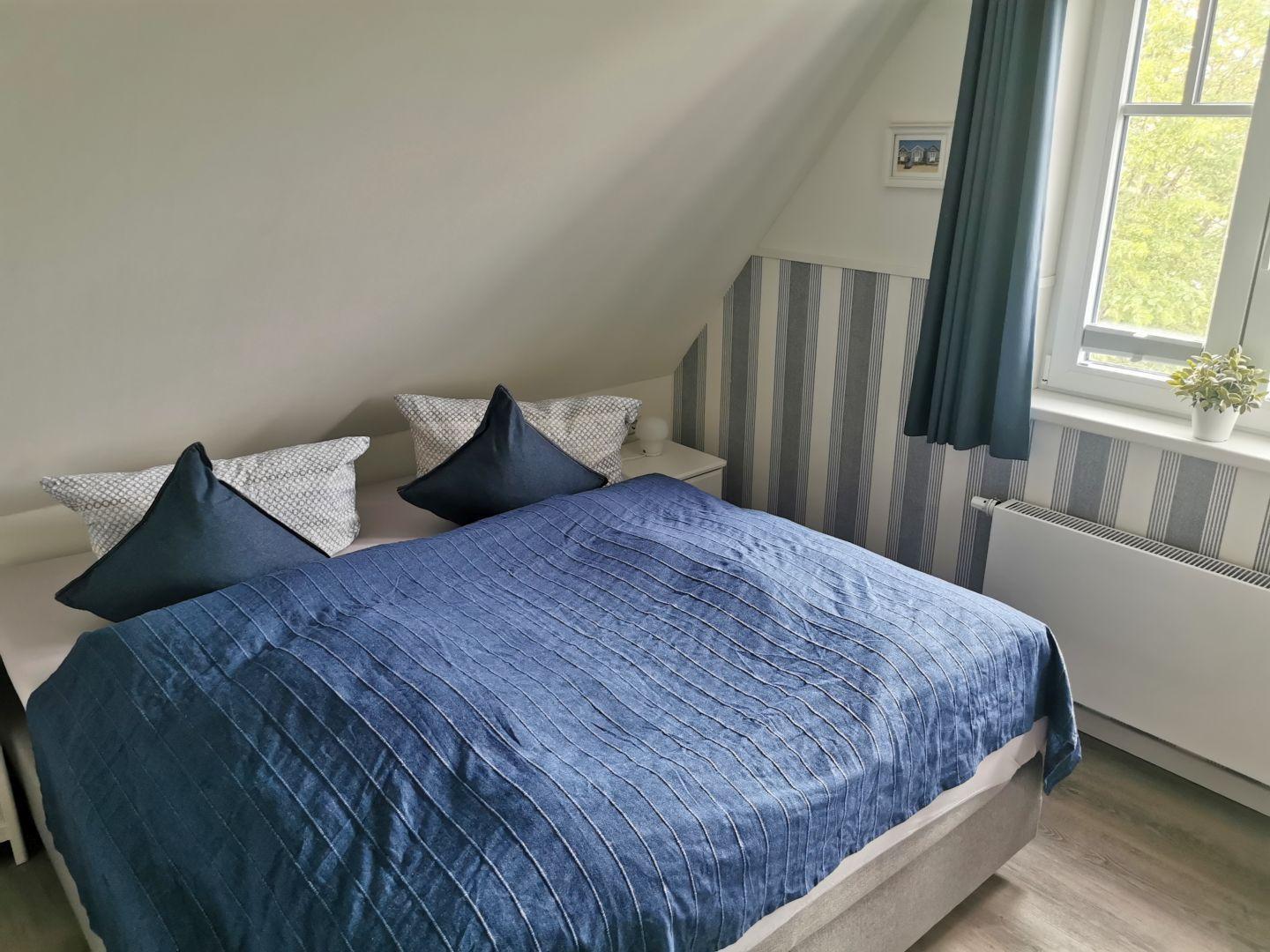 Helle Treppe mit Holzstufen und weißem Geländer. Im Hintergrund ist ein Wohnbereich mit Fenster und Sofa.