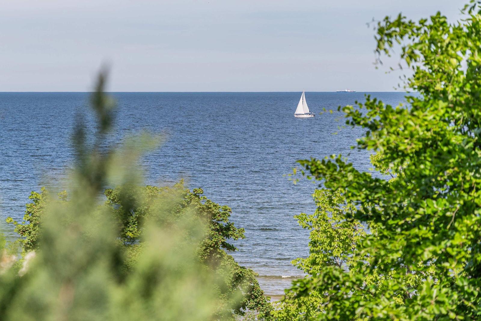Haus mit Balkon, Blick auf Meer und grüne Bäume. Holztor mit Schild.
