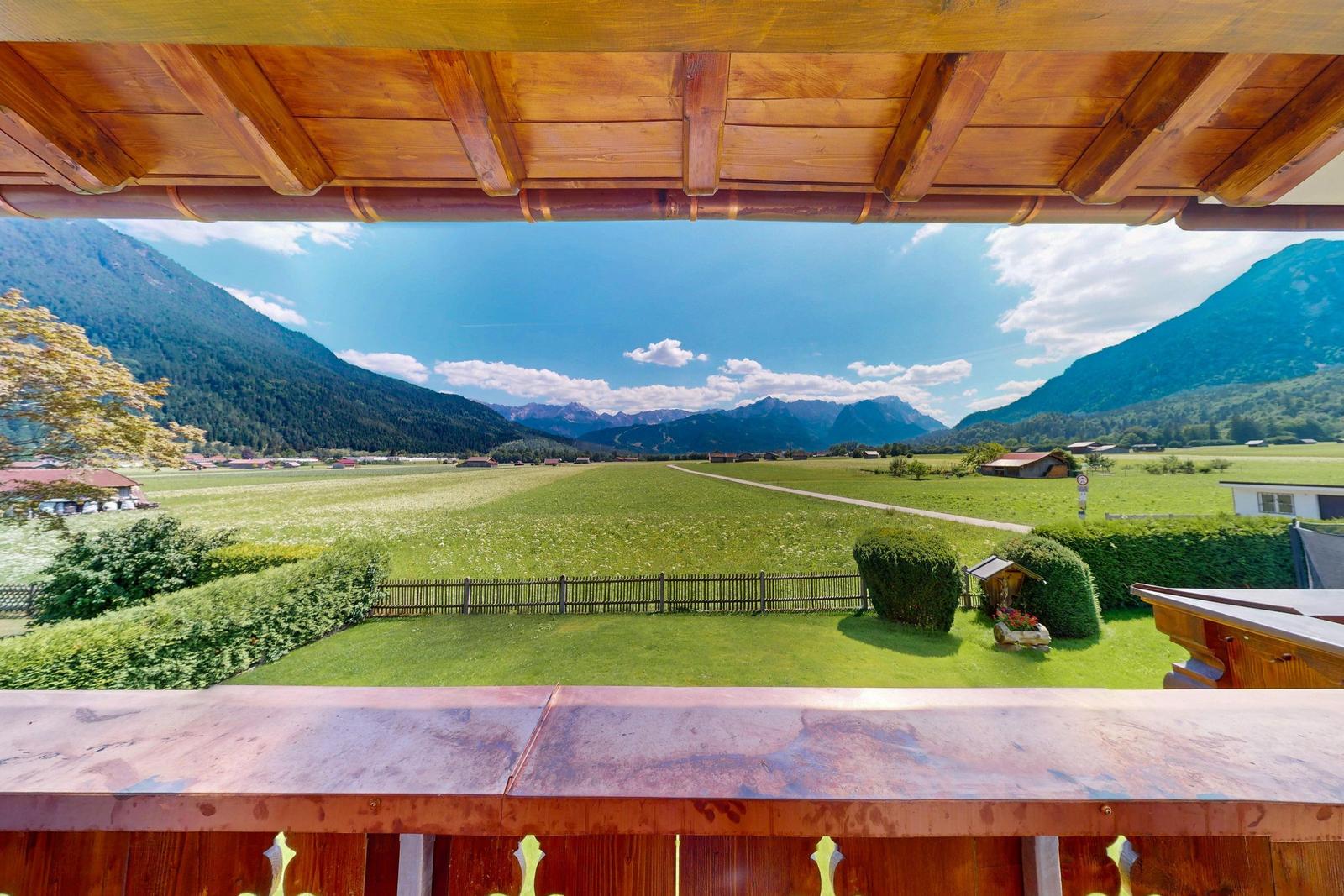 Terrasse mit Tisch und Stühlen, Blick auf grüne Wiesen und Berge.