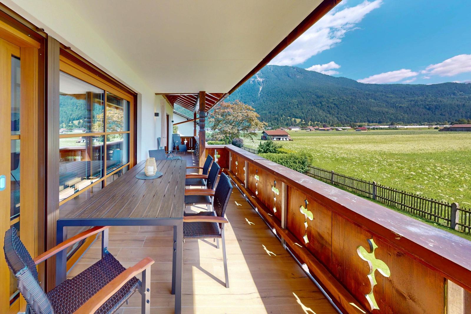 Terrasse mit Holzgeländer und Sitzgelegenheit. Blick auf grüne Wiesen und Berge.