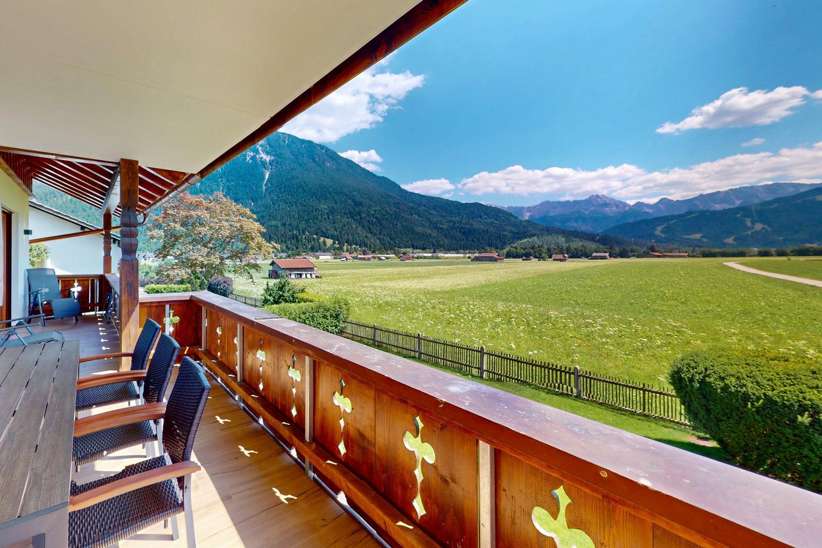 Terrasse mit Tisch und Stühlen, Blick auf Berge und Wiesen.