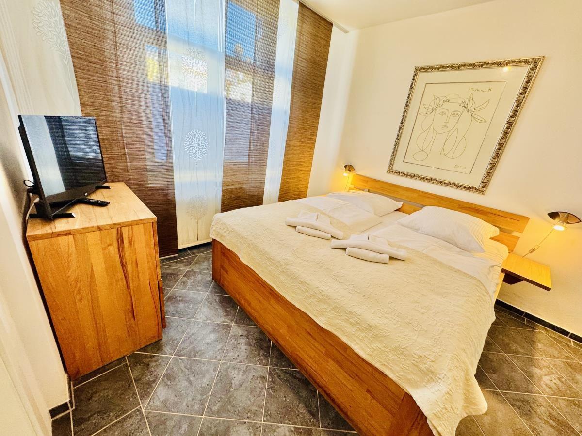 Schlafzimmer mit Holzbett, Fernseher und Fenster mit Vorhängen.