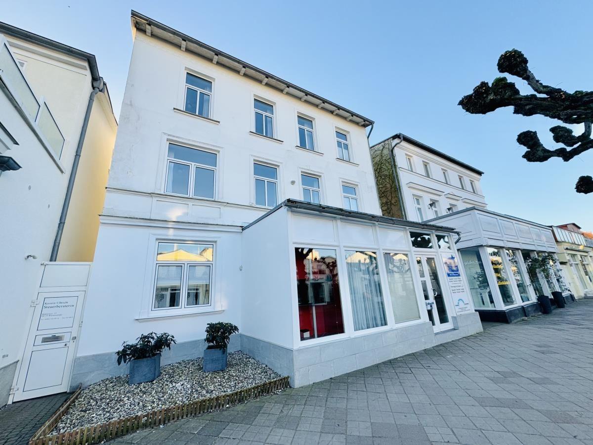 Ferienhaus mit Leuchtturm im Hintergrund und gepflastertem Platz.
