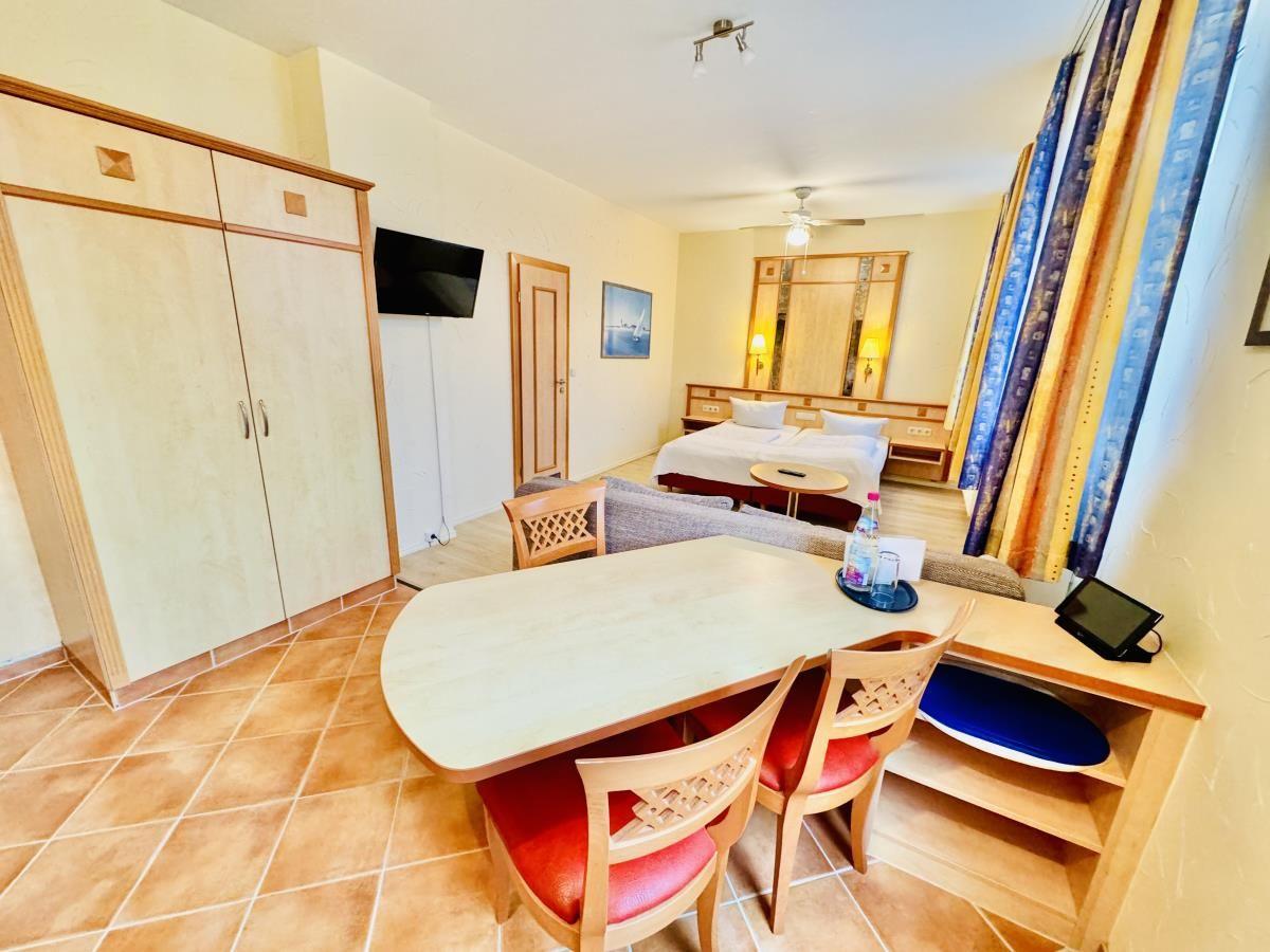 Zimmer mit Doppelbett, Sofa, Fenstern und Holzboden.