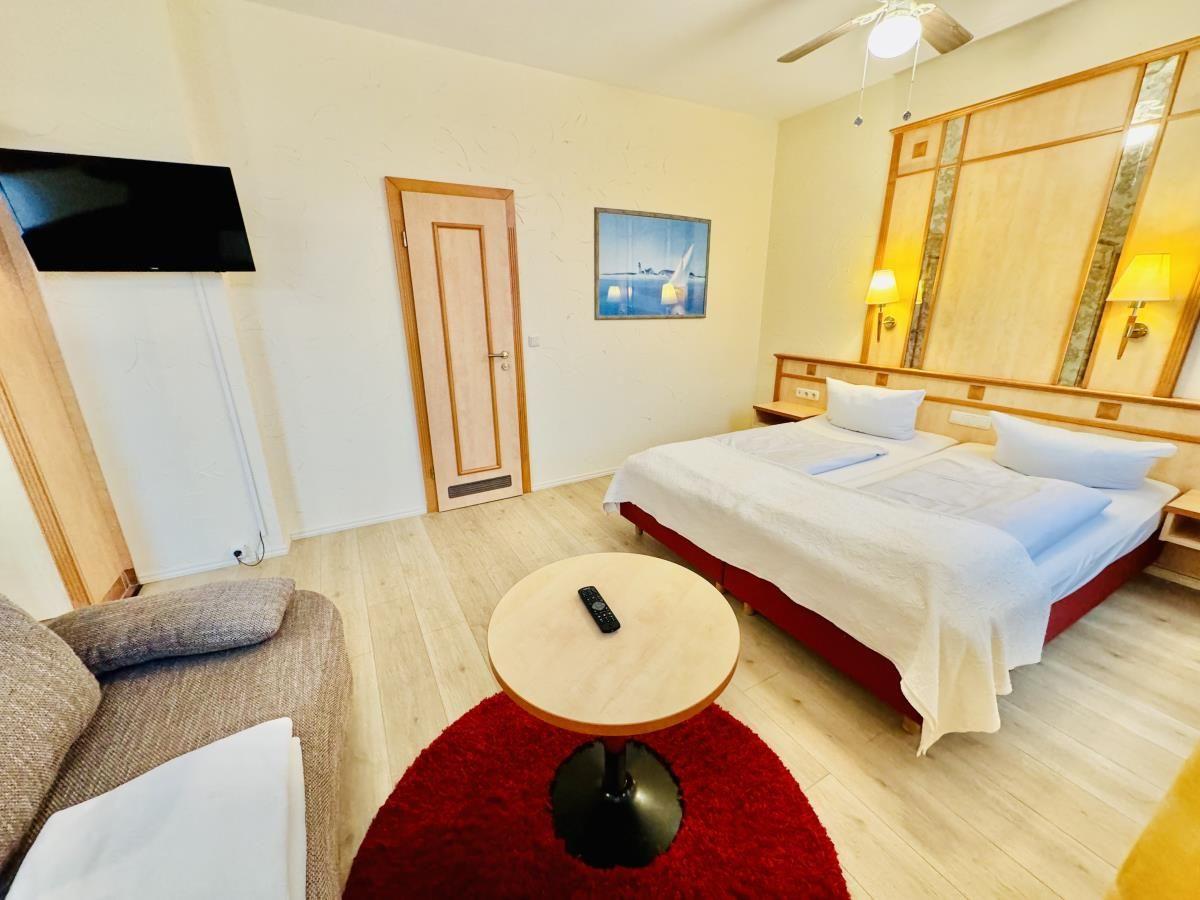 Schlafzimmer mit Doppelbett, Sofa und Küchenbereich im Hintergrund.