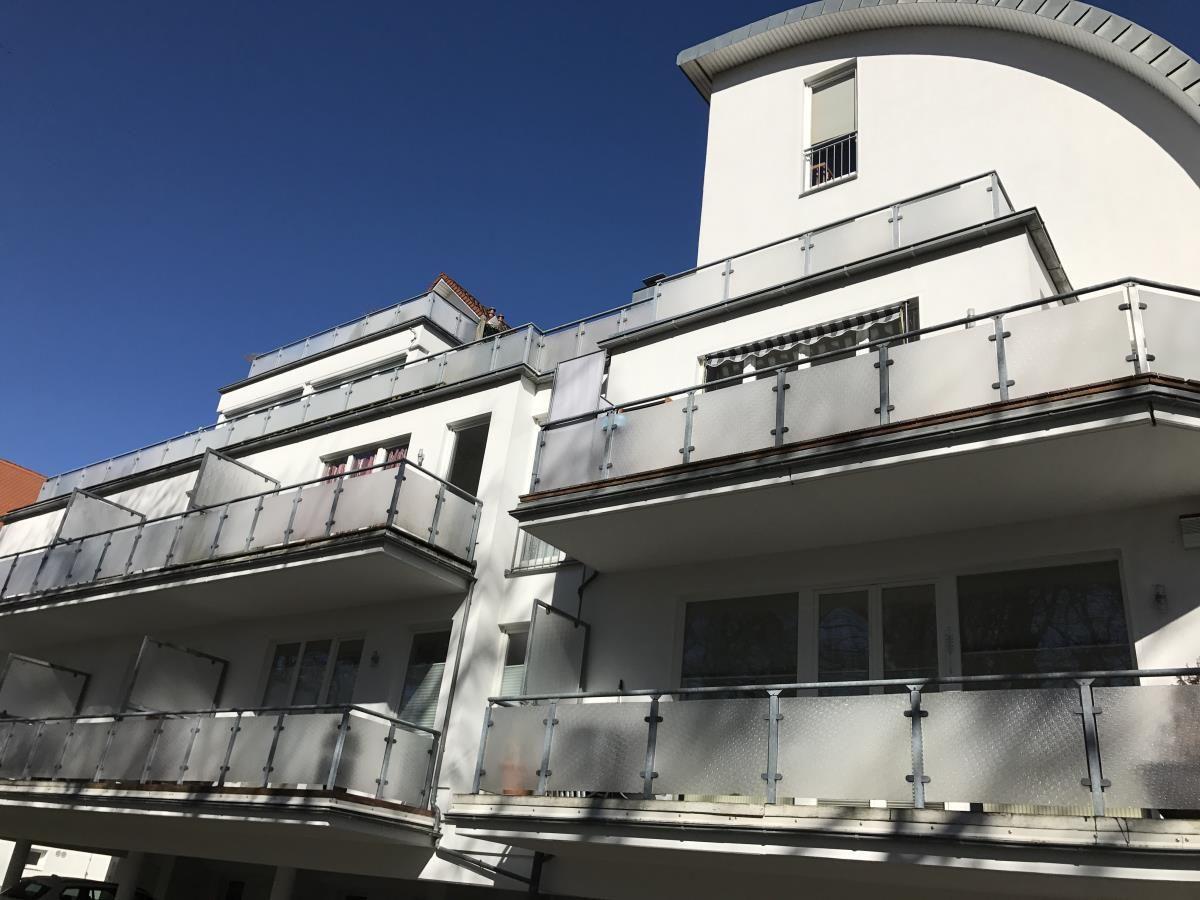 Pflasterter Hof mit Balkon und Parkplatz unter modernem Gebäude.