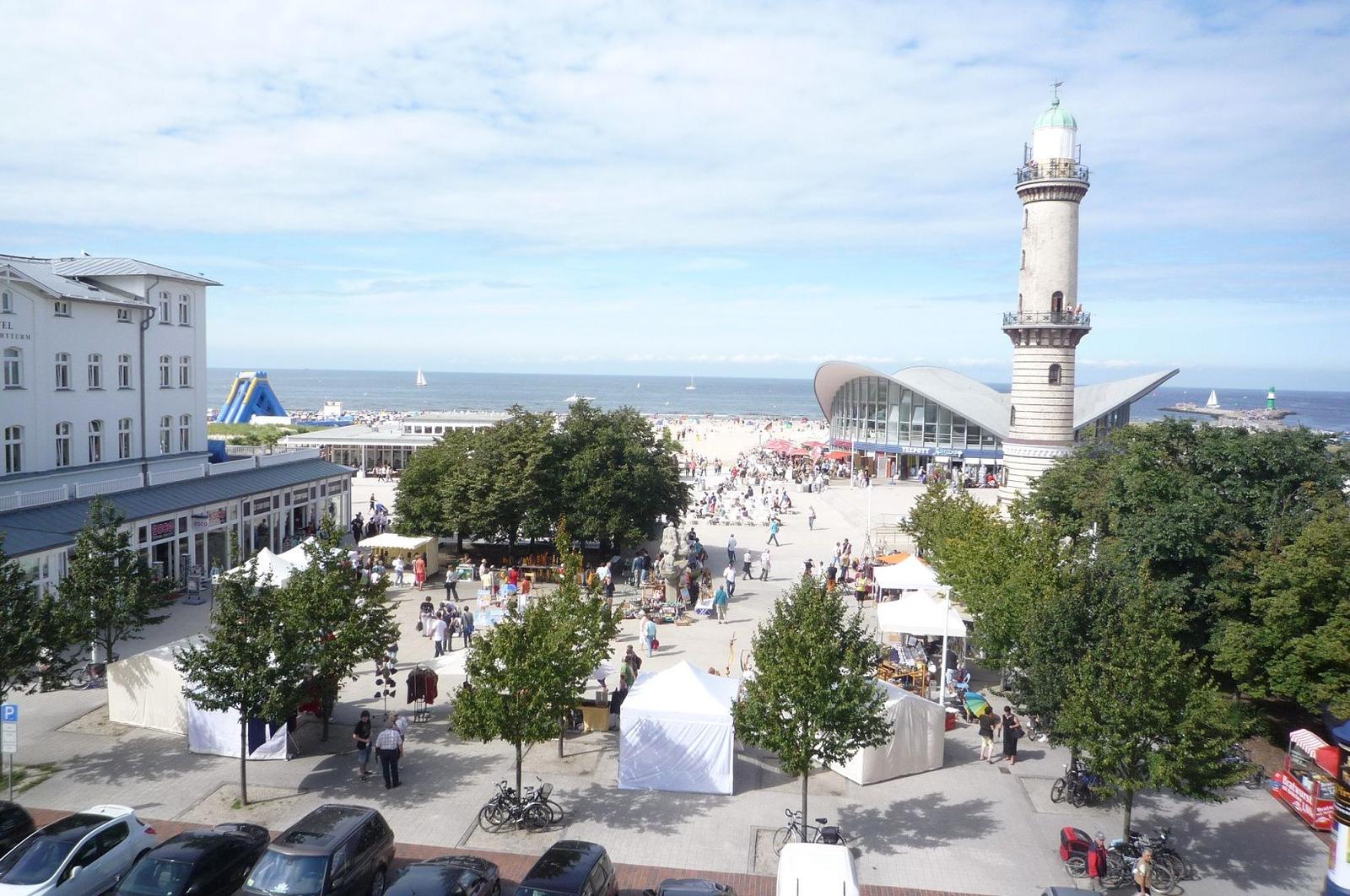 Ferienhaus in Warnemünde mit Leuchtturm im Hintergrund und gepflastertem Weg.