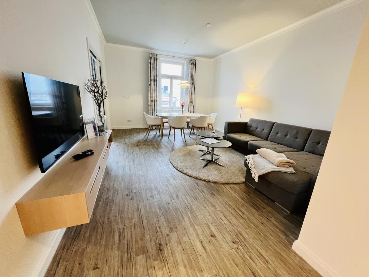 Wohn- und Essbereich mit grauem Sofa, runden Tischen und Holzboden.