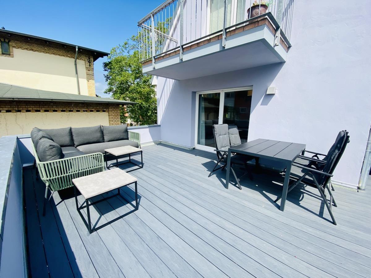 Terrasse mit zwei Liegestühlen und Tisch, angrenzende Fenster und Glastür.