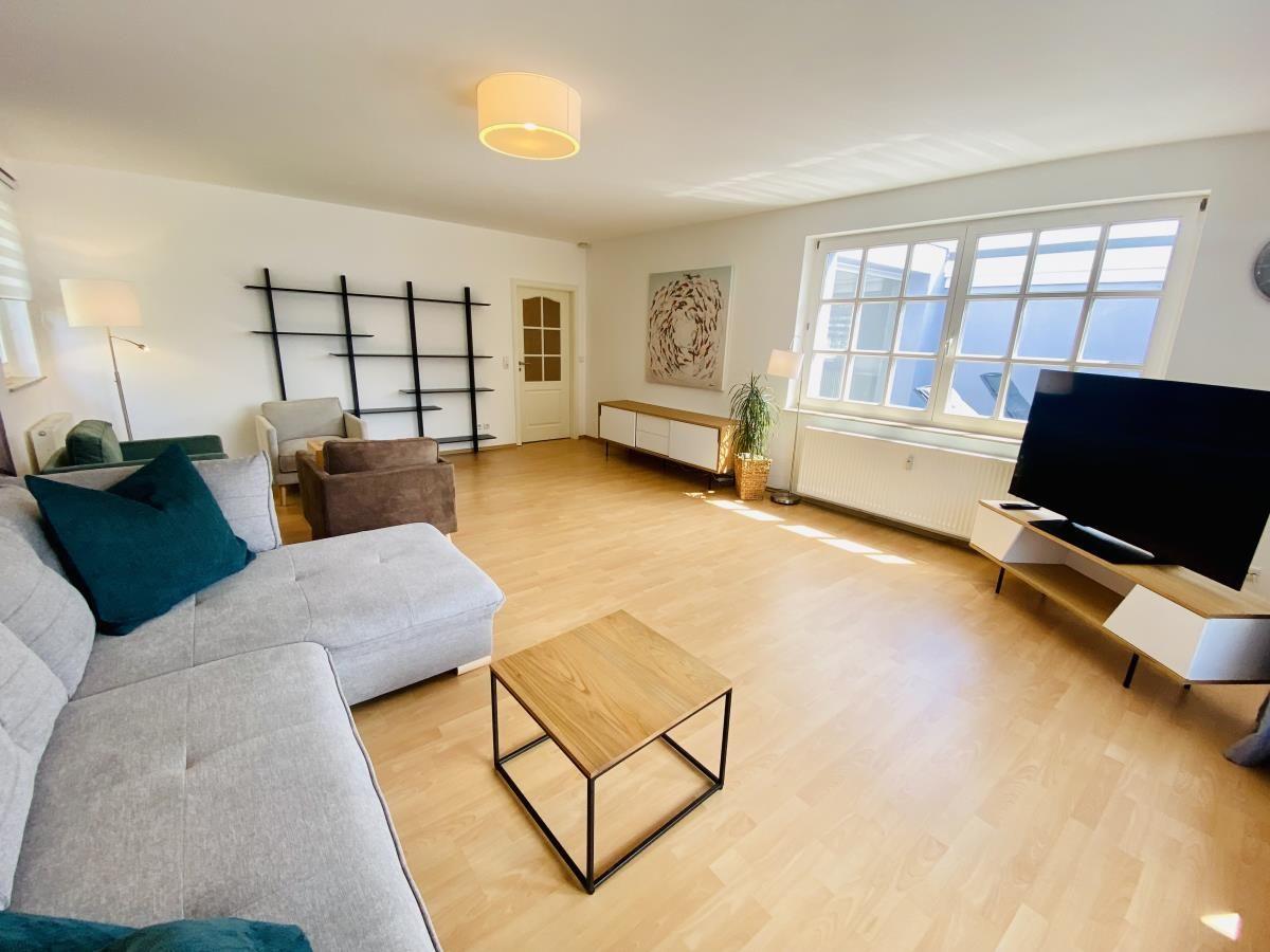 Wohnzimmer mit Sofa, Sesseln und Wandregal. Große Wanddekoration und Holzboden.