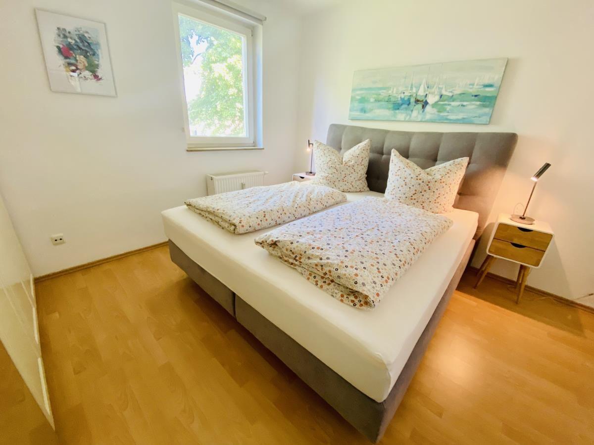 Doppelbett mit gemusterten Kissen und Decke, Wandbilder, Holzboden und Kleiderständer.