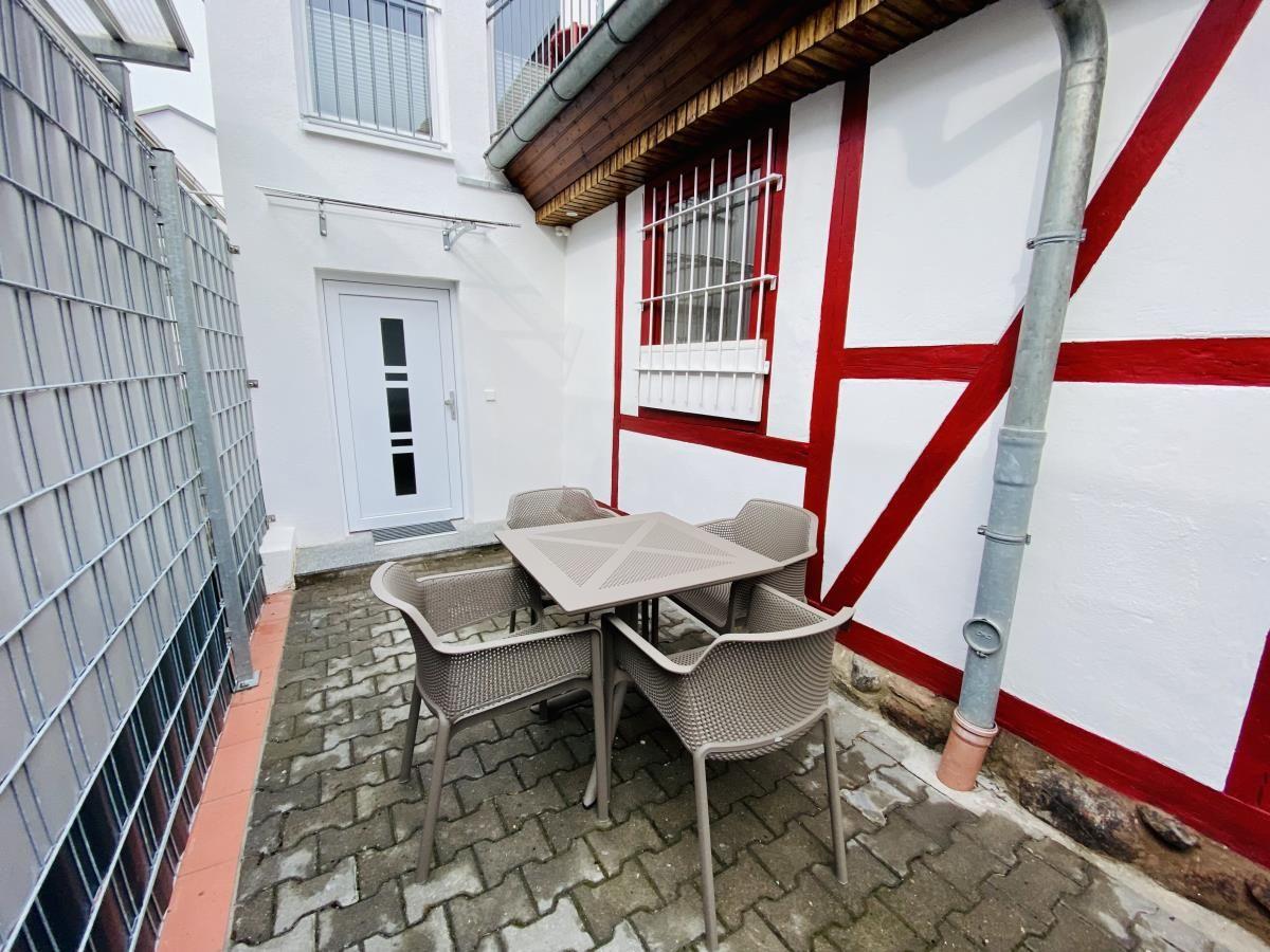 Terrasse mit zwei roten Stühlen und einem Tisch. Blick auf benachbarte Häuser.