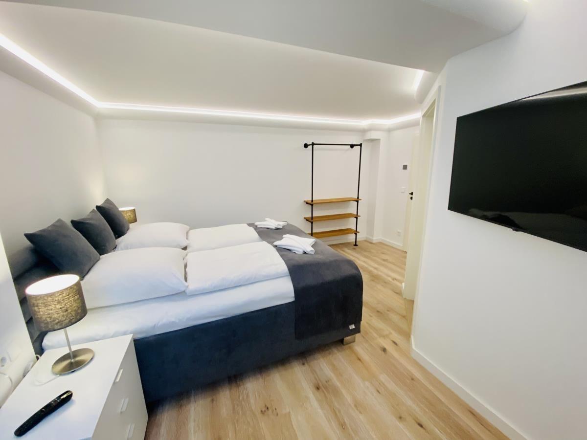 Schlafzimmer mit Bett, Nachttisch, Kleiderständer und Fernseher.