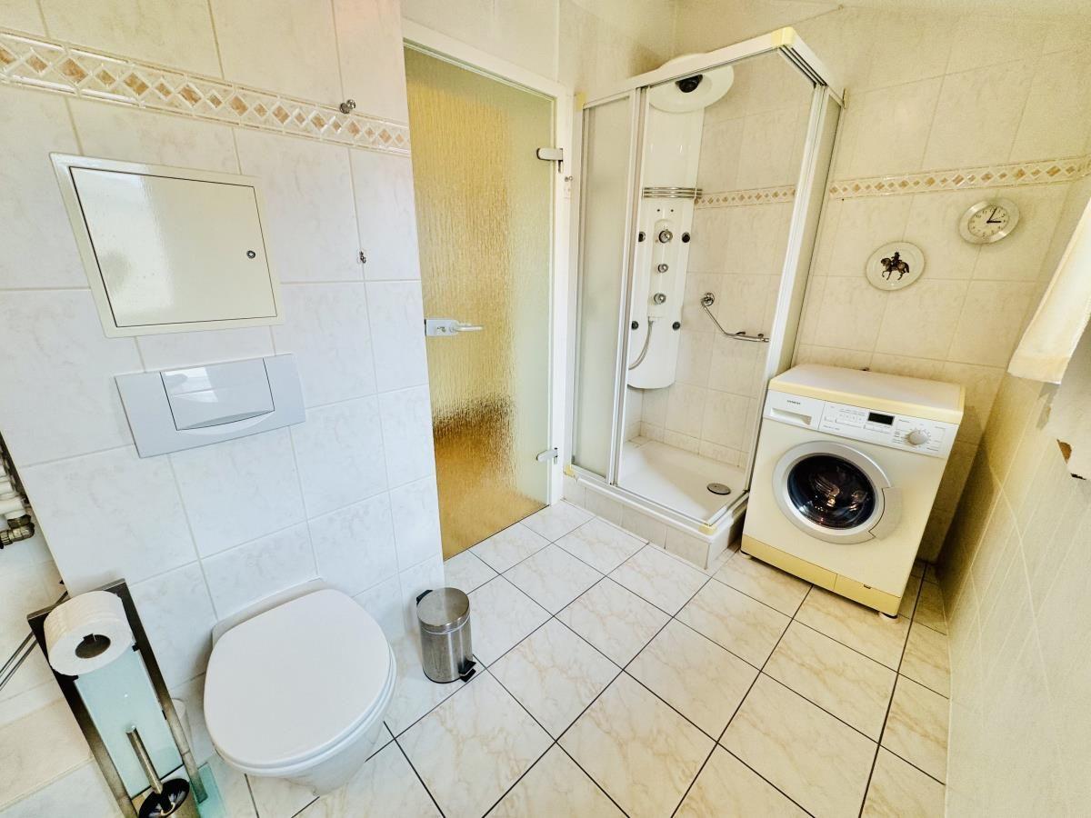 Badezimmer mit Waschbecken, Spiegel, Toilette und Heizung.