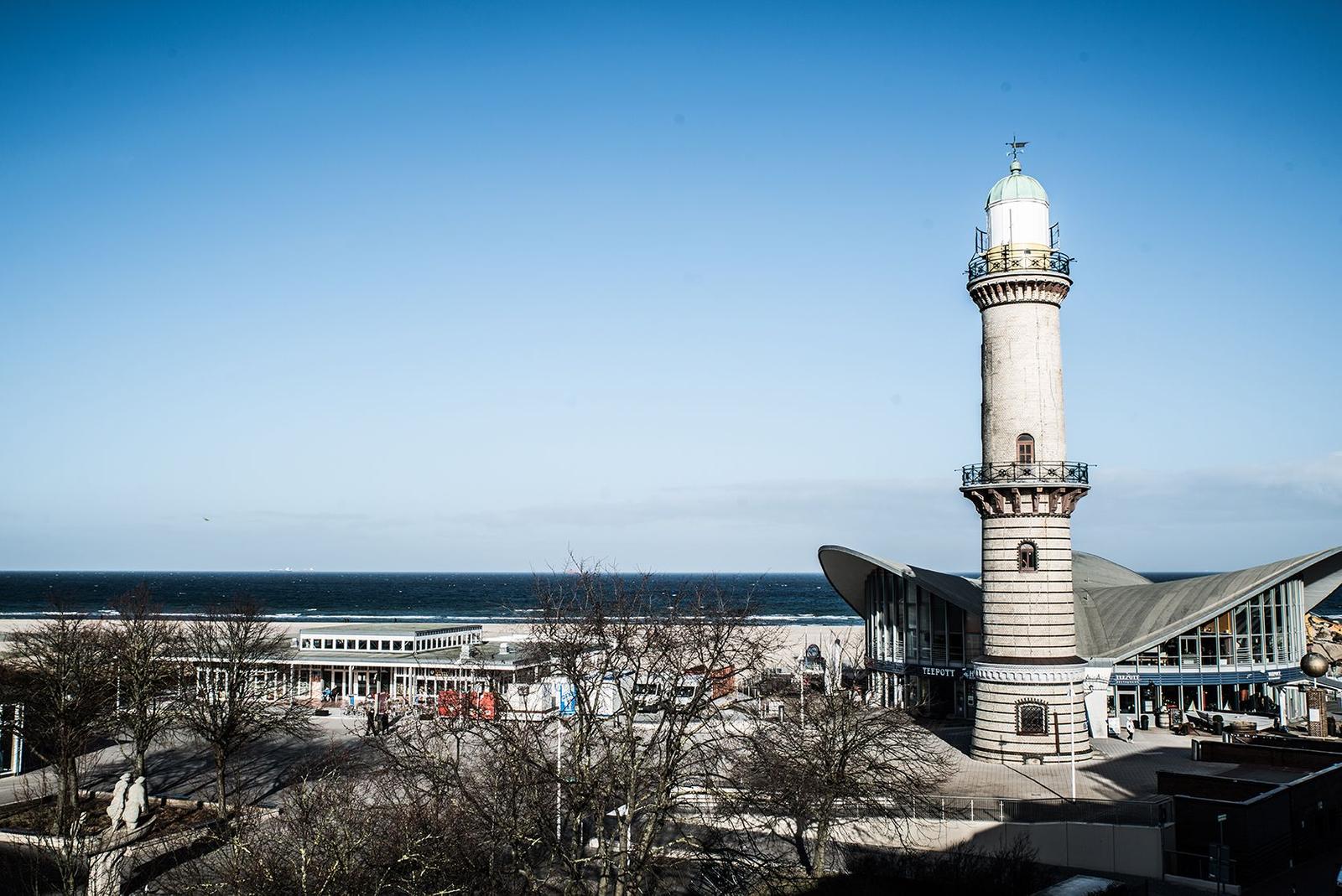 Balkon mit Sitzgelegenheit und Meerblick auf Leuchtturm und Strand.