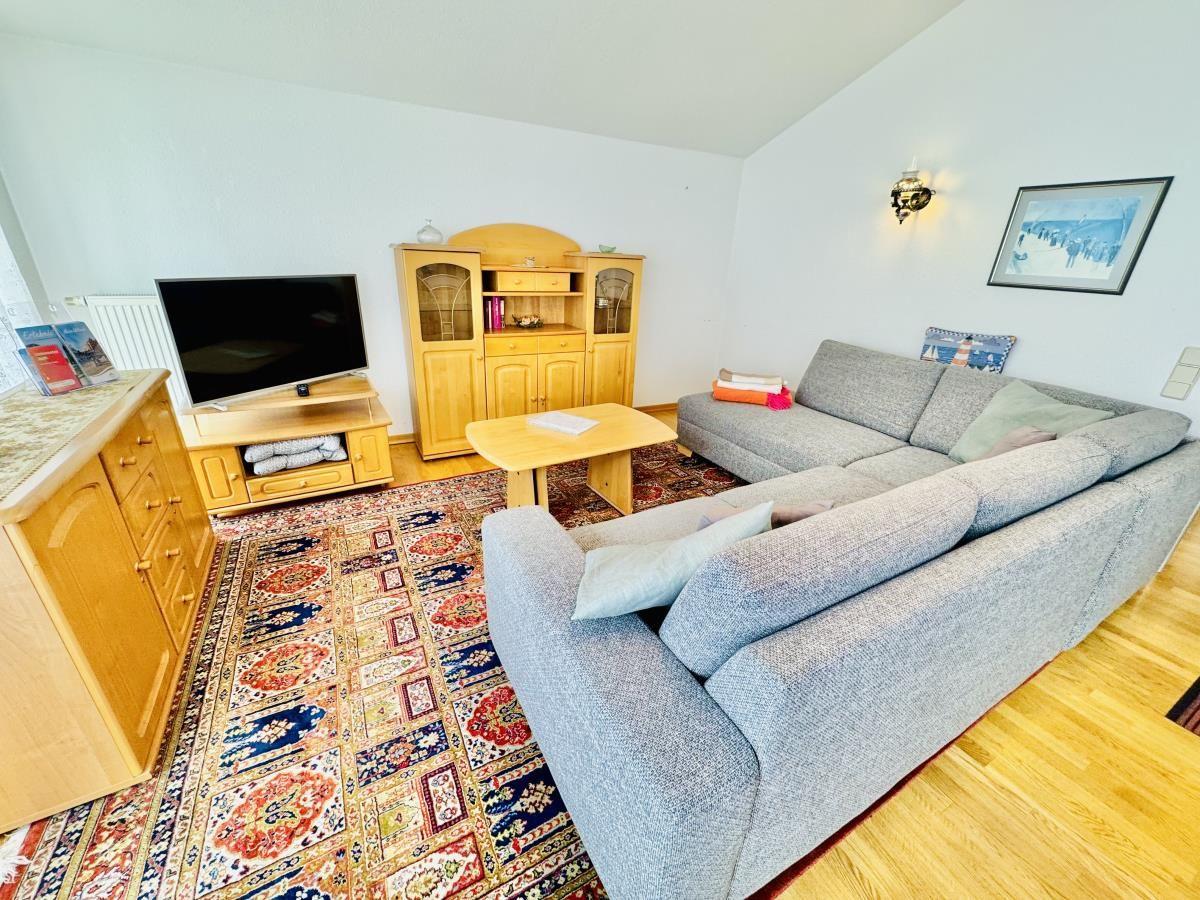 Essbereich mit Holztisch und Stühlen, Küchenbereich im Hintergrund, Holzboden und Fenster mit Vorhängen.