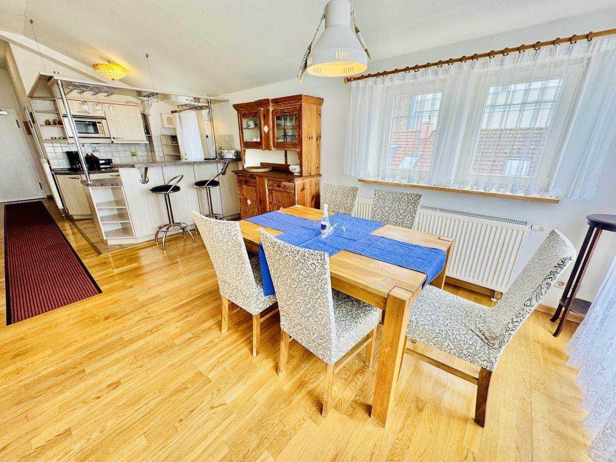 Essbereich mit Holztisch und Stühlen, Wohnbereich mit Sofa und Fernseher, Küche im Hintergrund.