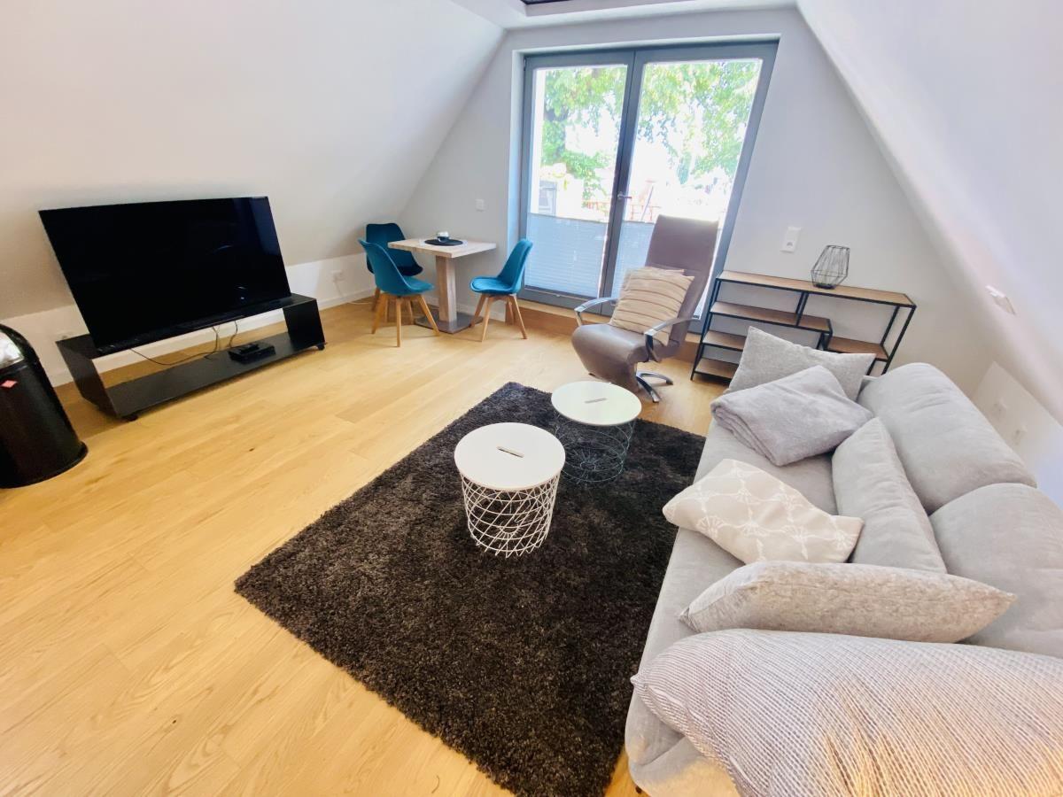 Wohnzimmer mit Sofa, Tisch, Stühlen und Fenster. Holzboden und Deckenbild.