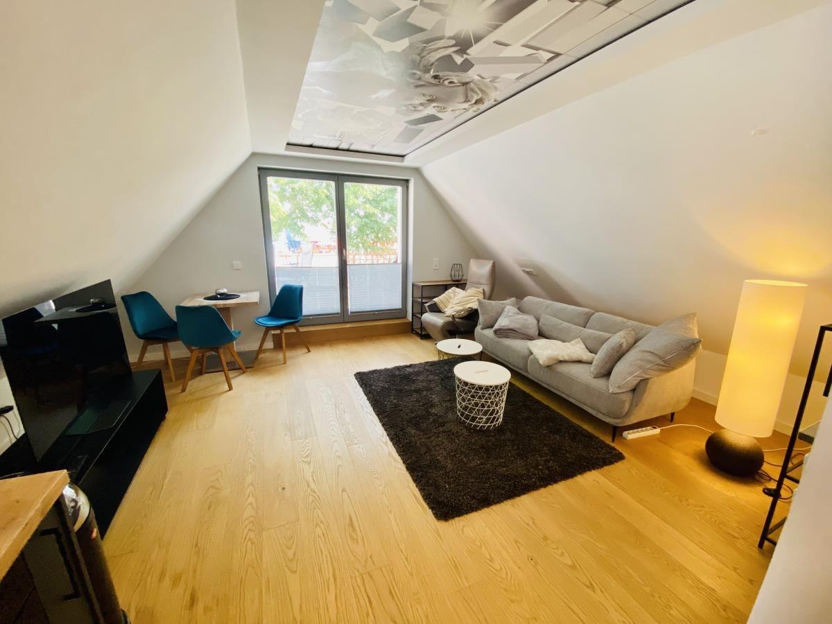 Wohnraum mit Sofa, Fernseher und Küchenzeile unter Dachschrägen.