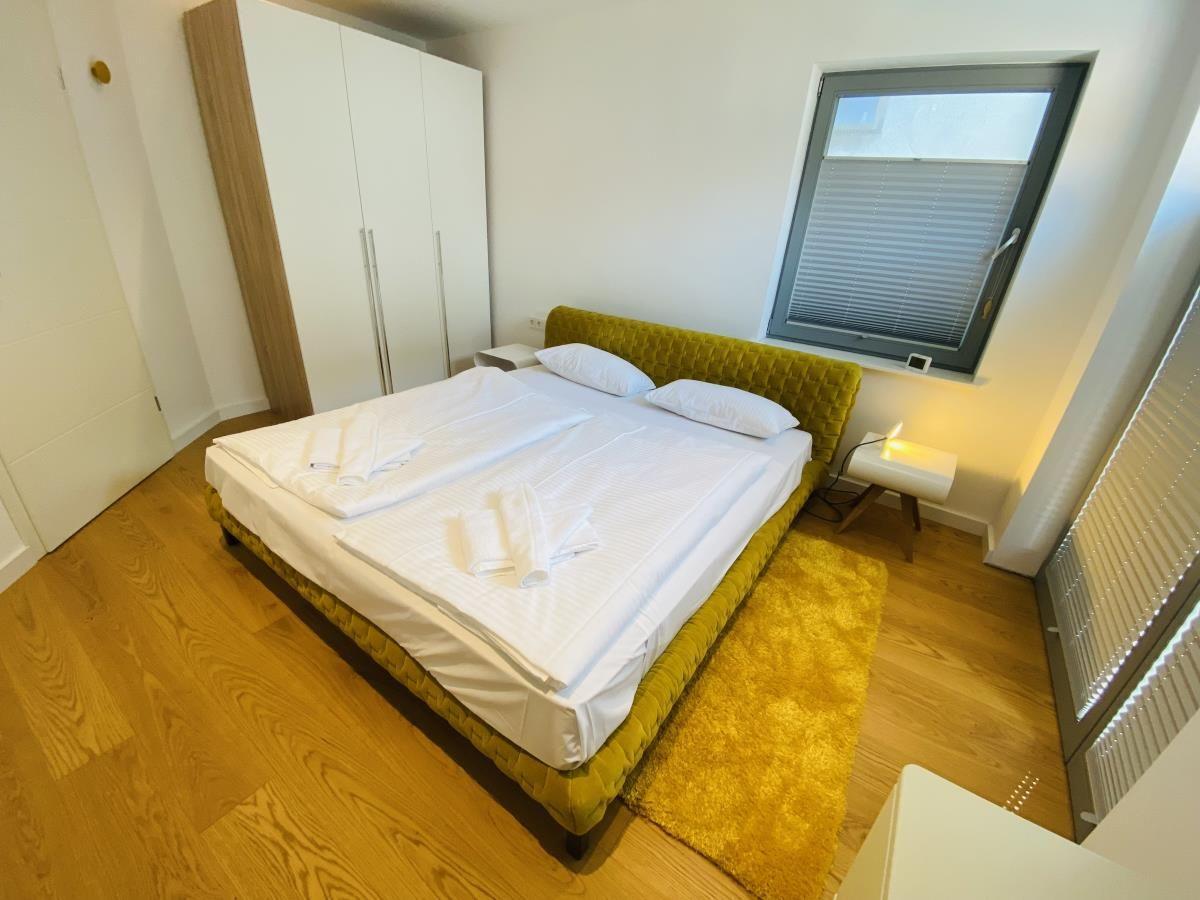 Wohnzimmer mit Sofa, Sessel, Teppich und Beleuchtung. Holzboden und Fenster sichtbar.