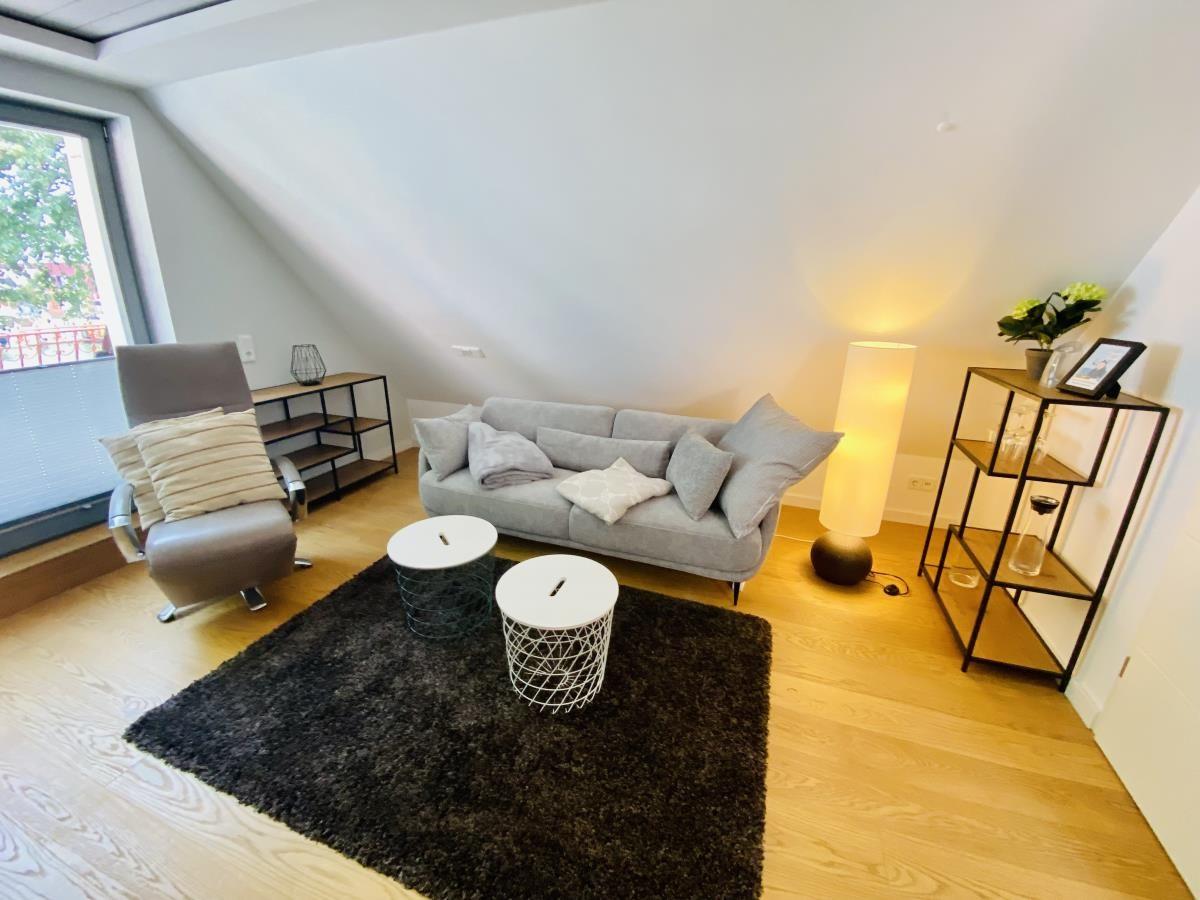Schlafzimmer mit Bett, Schreibtisch und Fenster. Holzboden und weiße Wände.