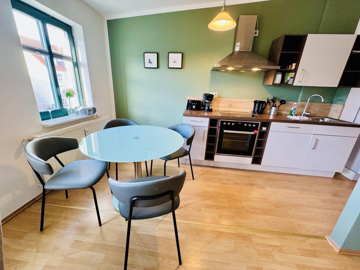 Küche mit Arbeitsplatte, Spüle und Kochfeld. Im Hintergrund Essbereich mit Tisch und Stühlen.