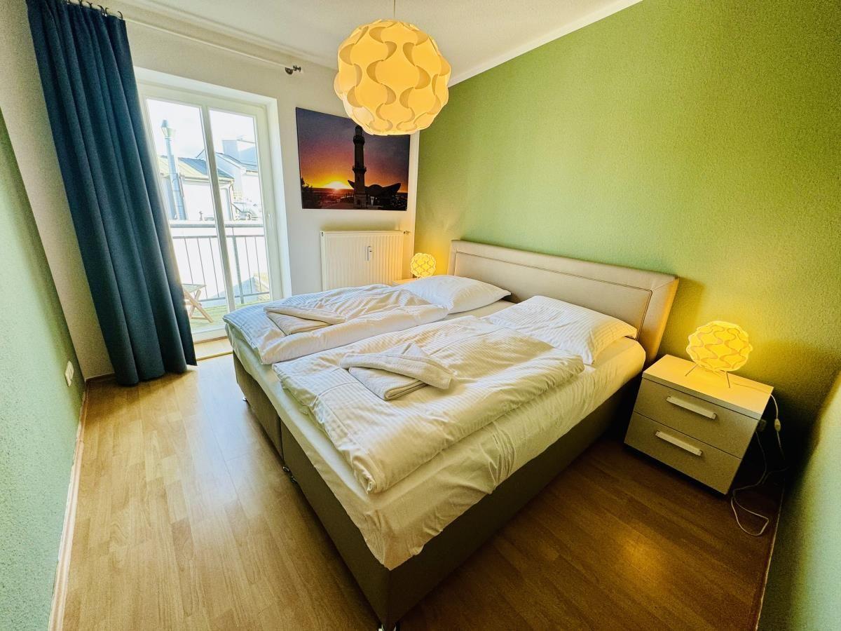 Schlafzimmer mit Bett, Nachttisch und Lampe an grüner Wand.