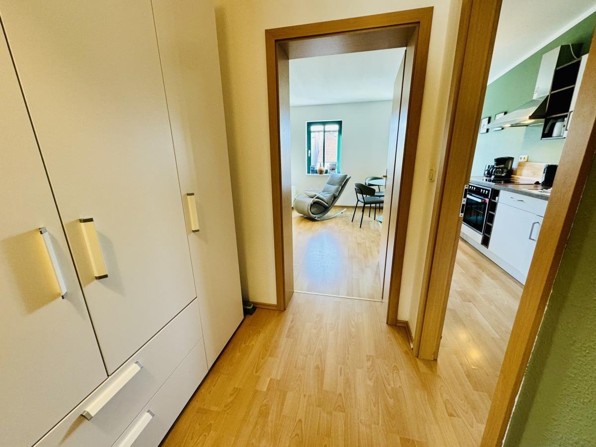Flur mit Holzboden, weißem Schrank und Blick in Schlafzimmer mit Bett und Balkon.