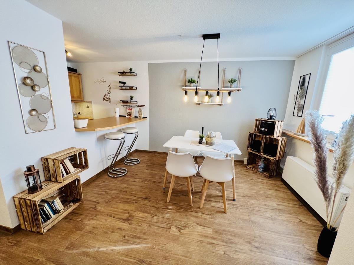 Essbereich mit weißem Tisch und Stühlen, offener Küche und Wohnzimmer im Hintergrund.