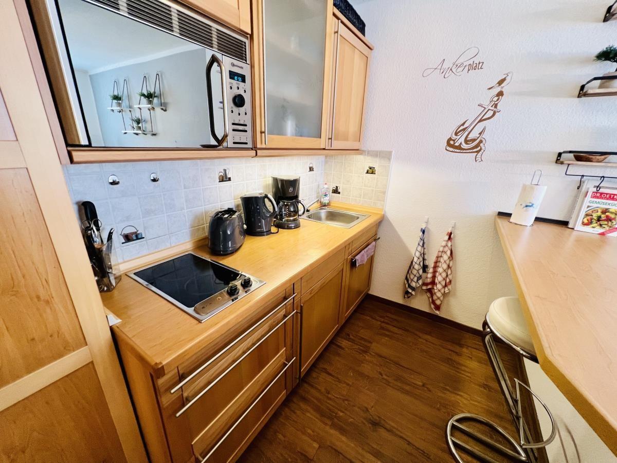 Wohn- und Küchenbereich mit Holzboden, Sofa, TV und Küchenzeile mit Barhocker.