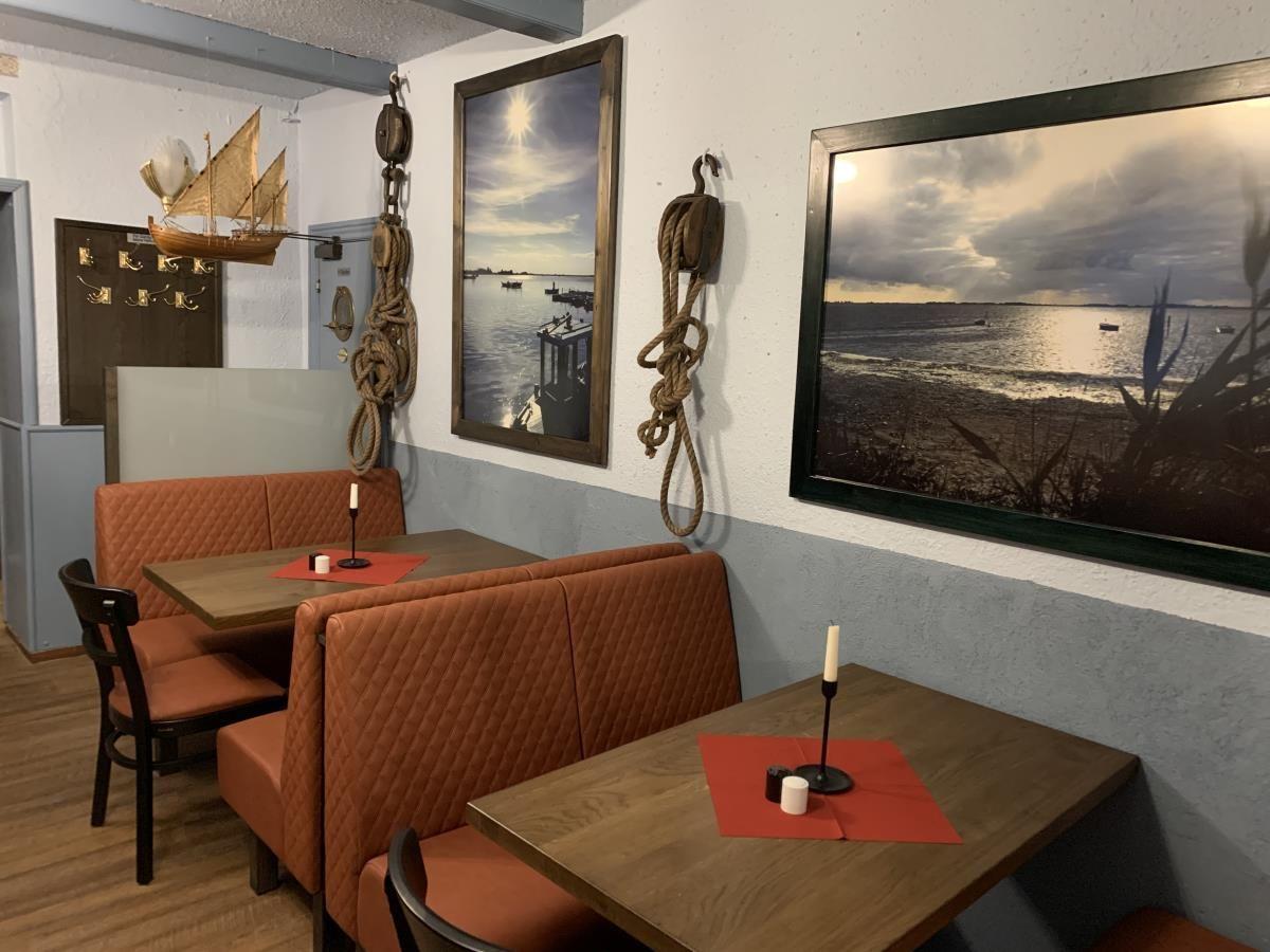 Raum mit Holztisch, Sitzbank und Fenstern mit Buntglasmotiven. An der Wand hängt ein Schädel.