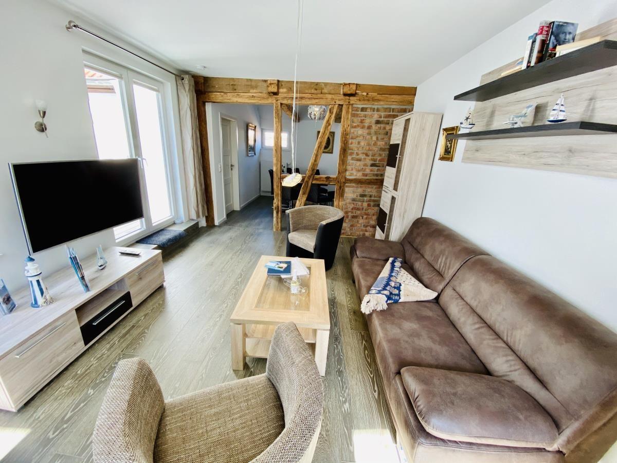 Küche mit Holzbalken, weißen Schränken und Holzboden. Durchgang zur Nachbarwohnung.