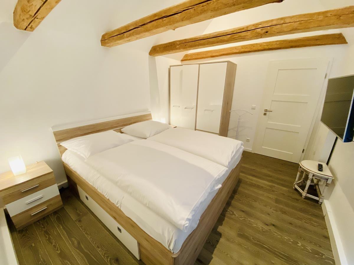 Schlafzimmer mit Doppelbett, Fernseher und Holzboden. An der Wand ein Gemälde.