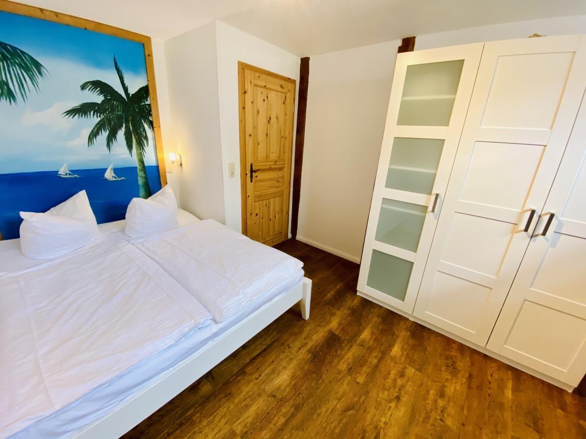 Schlafzimmer mit weißem Bett, Holzboden und Wandbild.