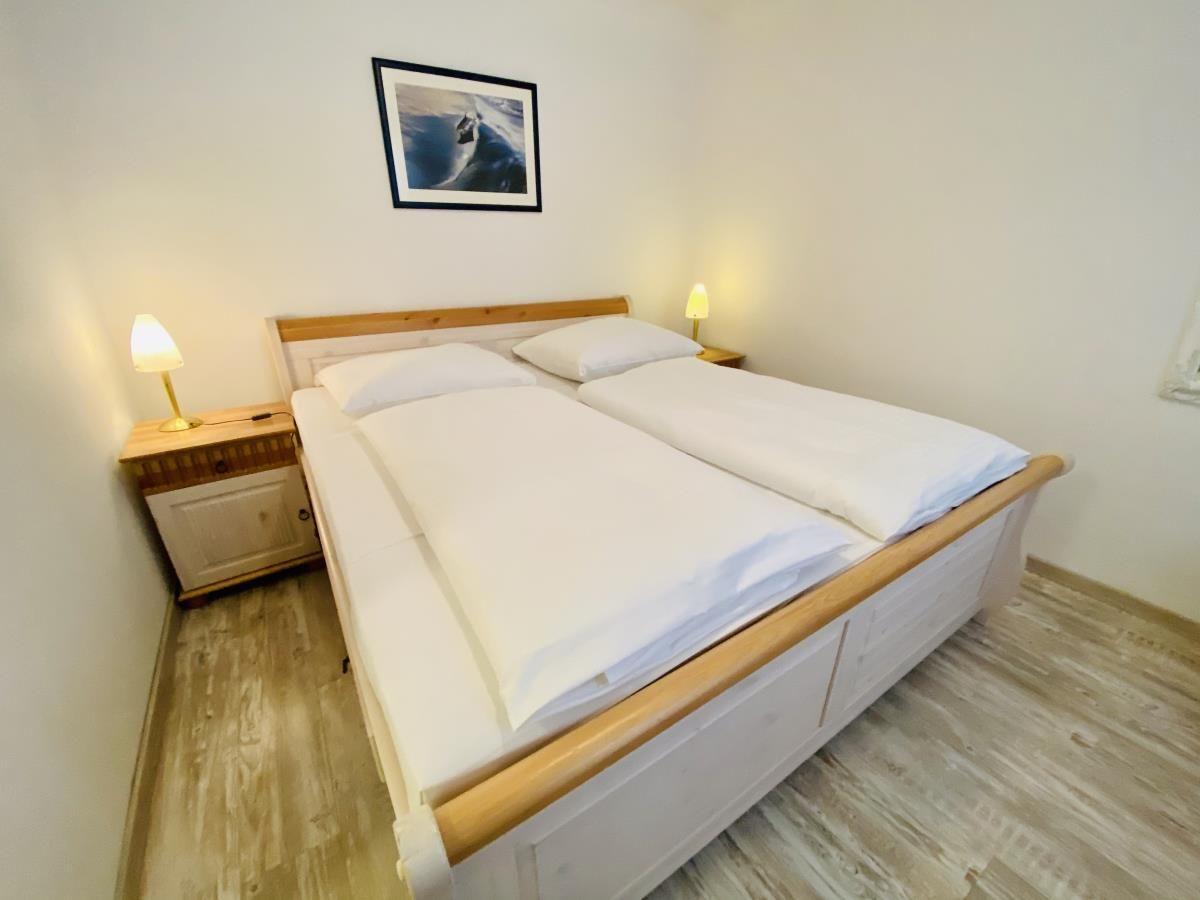 Schlafzimmer mit Bett, Kleiderschrank und Fenster. Tür führt in Bad.